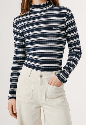 Femme portant un haut à manches longues rayé bleu marine et blanc et un pantalon taille haute blanc cassé, main dans la poche.