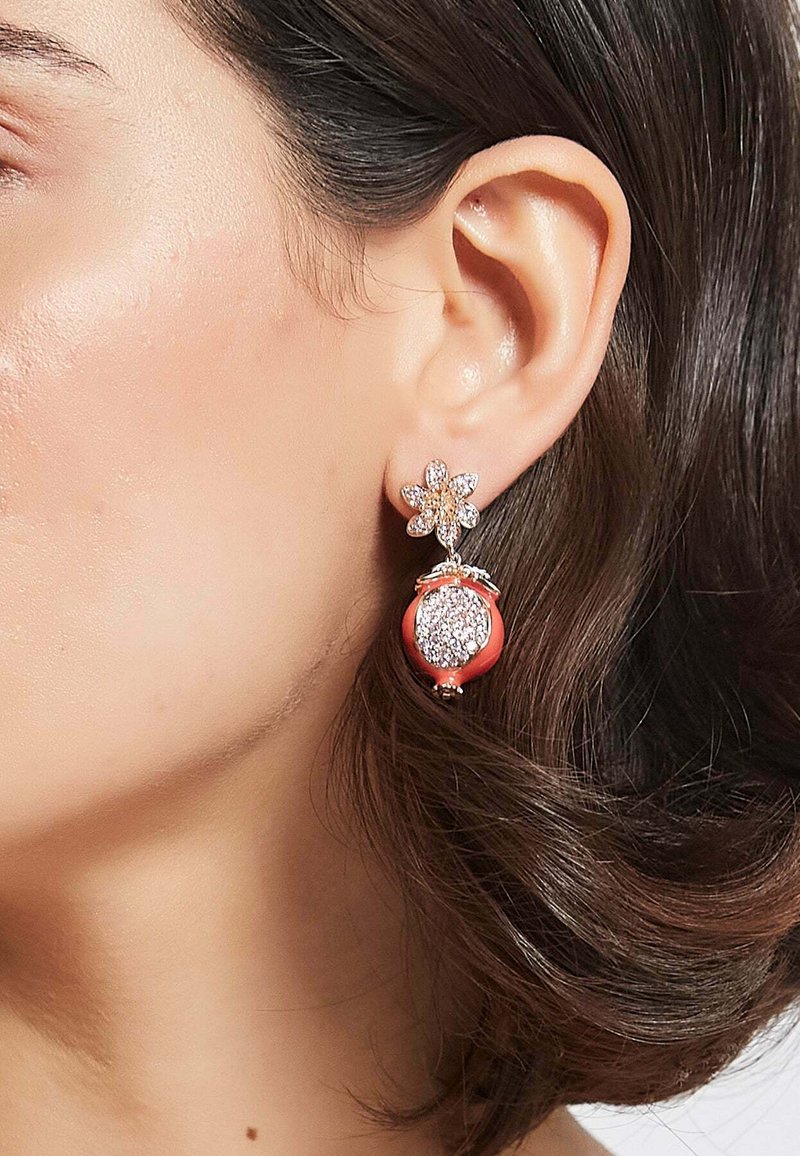 Orecchini in tono dorato caratterizzati da un design floreale con cristalli trasparenti nella parte superiore e un ciondolo di colore corallo decorato con una superficie testurizzata e scintillante.