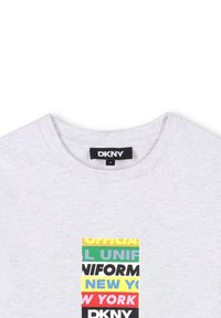 Camiseta de algodón gris con un estampado rectangular que presenta un texto multicolor: "UNIFORME OFICIAL NUEVA YORK" en diversas fuentes en negrita. Etiqueta de DKNY visible.