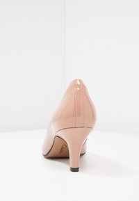 Chaussure à talon aigu en cuir verni nude avec un bout pointu et un talon fin, présentant des accents cousus et une semelle noire.