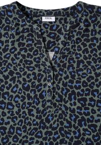 Blouse verte à col avec motif léopard noir et bleu et trois boutons bleu foncé sur la patte de boutonnage avant. L’étiquette indique "Cecil."