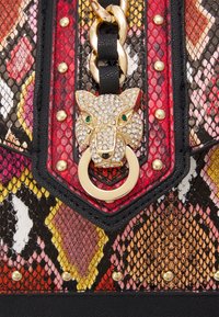 Sac à main coloré avec une texture effet peau de serpent en rouge, rose et jaune, équipé de ferrures dorées, d'une tête de lion décorative et d'accents à clous.