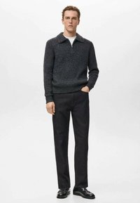 Suéter de punto gris oscuro con cuello tipo camisa y cremallera, combinado con pantalones negros y zapatos negros, sobre un fondo blanco liso.