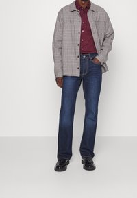 Koszula w kratę w odcieniach beżu i brązu, zestawiona z ciemnoniebieskimi dżinsami. Buty skórzane, czarne. Swobodny, warstwowy wygląd o luźnym kroju.