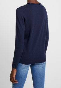 Suéter de punto azul marino con cuello redondo, mangas largas y dobladillo y puños acanalados. Se lleva con jeans de color azul claro.