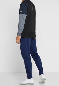 Sportoutfit mit einem langärmligen Oberteil in Schwarz und Grau mit Rundhalsausschnitt und einer Marineblauen Hose, gefertigt aus leichtem, atmungsaktivem Material.
