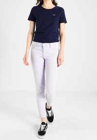 Námořnická modrá bavlněná tričko v kombinaci se světle fialovými slim-fit džíny. Model má na sobě černobílé tenisky. Jednoduchý design, bez vzorů nebo akcentů.