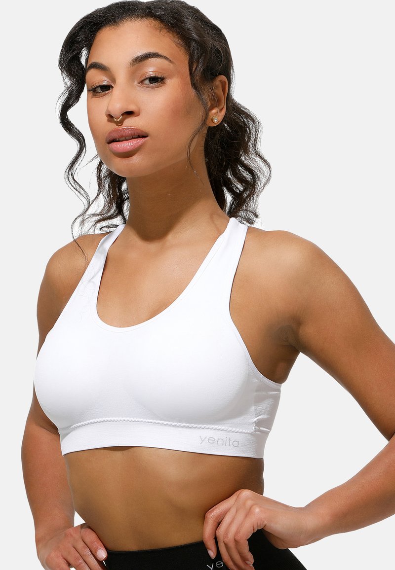 Brasile sportivo bianco con scollatura a barca, spalline spesse, texture liscia e dettaglio di marca sottile sulla fascia. Adatto per l'abbigliamento attivo.