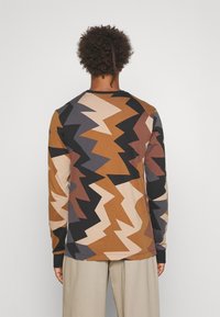 Koszula z długim rękawem z bawełny, z geometrycznym wzorem w zygzaki w odcieniach brązu, czerni, beżu i taupe. Dekolt w kształcie crew neck.