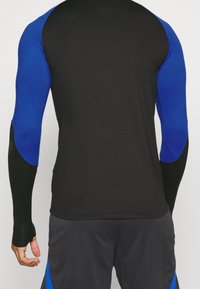 Langärmliges Sportshirt in Schwarz mit blauen Akzenten. Verfügt über eine glatte Textur und eine formschlüssige Passform. Schwarze strukturierte Ärmel fügen Detail hinzu.