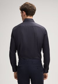 Dunkelblaues Langarmhemd aus strukturiertem Stoff. Es hat einen klassischen Kragen, Knopfmanschetten und ein gerades Rückendesign.