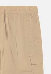 Beiga cargoshorts gjorda av lättviktsmaterial, med elastisk midja, dragsko och flera fickor med sömdetaljer.