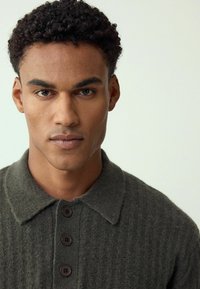 Zielona prążkowana dzianinowa koszulka polo z zapinanym na guziki kołnierzykiem i trzema brązowymi guzikami, wykonana z teksturowanej wełny.