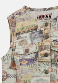 Gilet in denim senza maniche con una stampa pubblicitaria colorata e retrò. Presenta bottoni in metallo e un colletto rotondo. Varie scritte visibili.