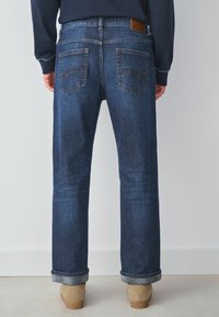 Jeansy z ciemnogranatowego denimu o prostym kroju, z dwoma tylnymi kieszeniami i skórzaną naszywką marki na pasku. Nogawki nieobszyte.