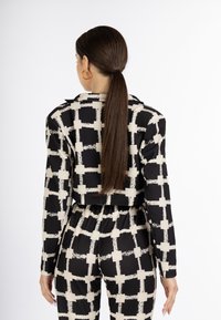 Ingekorte zwart en crème geblokte jas met lange mouwen, voorzien van een puntige kraag en textuur patroon. Gestyled met bijpassende broek.