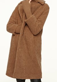 Brauner, flauschiger Mantel aus strukturiertem Stoff mit Reverskragen und gerippten Ärmeln. Hat eine lockere Passform und eine Frontknopfverschlus.