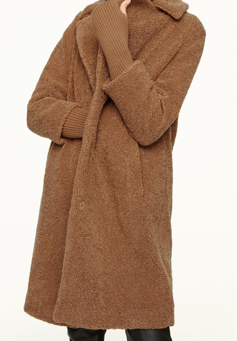 Brauner, flauschiger Mantel aus strukturiertem Stoff mit Reverskragen und gerippten Ärmeln. Hat eine lockere Passform und eine Frontknopfverschlus.