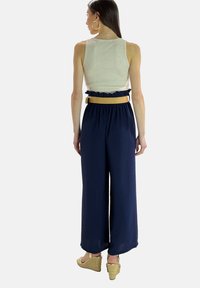Lichtgrijze tanktop gecombineerd met marineblauwe wijde broek met een gerimpelde elastische taille en een strokleurige riem. Sleehakken maken de outfit compleet.