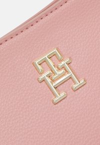 Růžová strukturovaná kůže s geometrickým zlatým logem s výrazným designem dvojitého "H". Materiál má měkký, zrnitý vzhled.