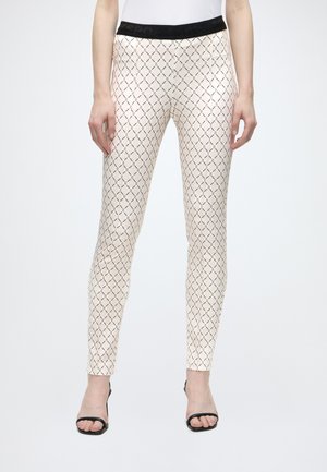 Pantaloni beige slim fit con motivo geometrico nero, vita elastica nera, indossati con tacchi aperti neri.