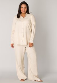 Beige, long-sleeve button-up shirt with a chest pocket, paired with loose-fitting beige trousers; fabric appears soft and lightweight.