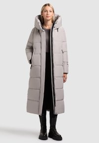 Lungo cappotto grigio imbottito con cappuccio, caratterizzato da un design trapuntato, due tasche laterali e una chiusura frontale a zip lungo tutto il corpo.