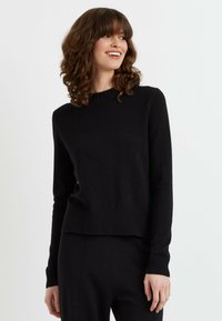 Pull en maille noir avec un col et un ourlet côtelés, doté de manches longues et d'une coupe décontractée. Texture lisse et détails de design minimalistes.