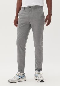 Pantalones a cuadros grises de corte ajustado, con cierre de botón y bolsillos laterales, combinados con zapatillas deportivas plateadas y azules.