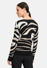 Schwarzer Pullover mit wellenförmigen Mustern in Creme und Beige. Mit weitem Ausschnitt und gerippten Bündchen. Weiche Stricktextur.