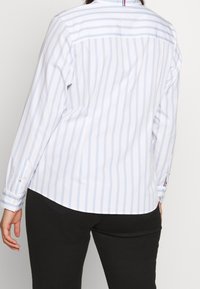 Langærmet skjorte i hvid med lyseblå striber, med spidst krave og knaplukning ved manchetterne. Glat, vævet stof med en buet kant.