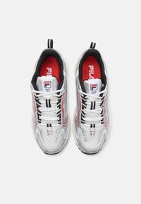 White and silver sneakers with black accents, red lining, mesh upper, and thick soles. Features logo and contrasting stitching details.