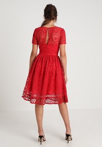 Rotes Spitzenkleid mit tailliertem Oberteil, kurzen Ärmeln und schwingendem Rock. Hat einen Schlüssellochausschnitt auf der Rückseite und einen fransigen Saum.