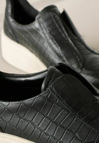 Schwarze Slipper aus strukturiertem Leder mit einem Krokodil-Muster, ausgestattet mit einer weißen Plattformsohle.