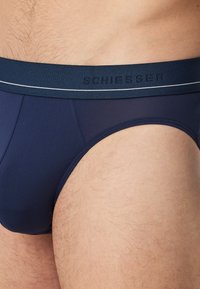 Marinblå herrbrief med elastiskt midjeband som har "SCHIESSER"-logotyp och vit kant. Slät textur, figurnära design.