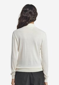 Vit lättviktig tröja med långa ärmar, ribbad muddar och nederkant. Mjuk textur och enkelt mönster, med detaljer i kragen.