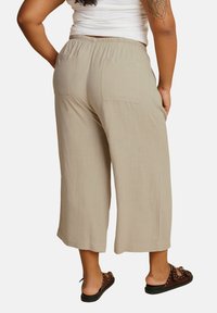 Lichtbeige, cropped broek met een elastische tailleband, voorzien van twee achterzakken. Gladde textuur, lichtgewicht stof, gecombineerd met donkere instappers.