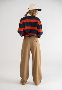 Gestreepte marineblauwe en oranje trui met een losse pasvorm, gecombineerd met beige wijde broekspijpen. Heeft een honkbalpet met een groene klep.