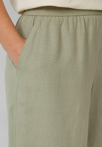 Lichtgroene broek gemaakt van een zachte, gestructureerde stof met een elastische tailleband en zijzakken. Visueel eenvoudige en comfortabele uitstraling.