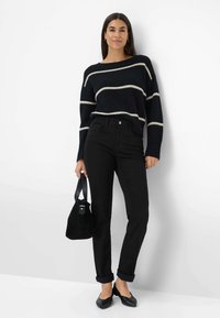 Pull noir à rayures avec une coupe lâche, associé à un jean noir. Les accessoires incluent un petit sac et des ballerines noires. Design et textures simples.