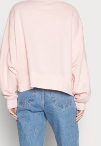 Ljust rosa cropped sweatshirt med nedhasade axlar, ribbade muddarna och en mjuk textur, kombinerad med högmidjade blå denimjeans.