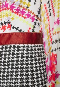 Robe colorée présentant des motifs floraux abstraits audacieux en rose, jaune et orange, avec un bas en pied-de-poule noir et blanc et une ceinture en velours.