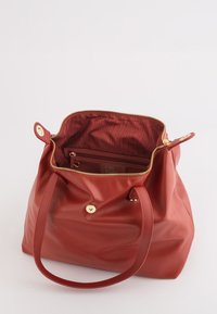 Sac à main en cuir rouge doux avec une fermeture éclair dorée et un fermoir à pression, partiellement ouvert montrant un intérieur en tissu rayé et une poche zippée.