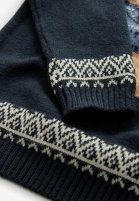 Navyblaues Strickpullover mit einem strukturierten weißen Musterband am Ärmelbündchen, das am Rand eine gerippte Stricktextur aufweist.