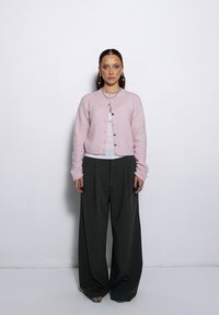 Jasnoróżowy, puszysty kardigan z okrągłym dekoltem i zapięciem na guziki, w połączeniu z szerokimi, ciemnoszarymi spodniami. Dodatki to naszyjnik warstwowy.