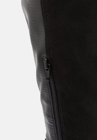 Detailní záběr na černou botu s texturovaným vzorem na boku a černým zipem, který probíhá svisle podél švu.