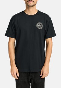 Schwarzes Baumwoll-T-Shirt mit einem runden weißen Logo auf der linken Brustseite, kurzen Ärmeln und einem standardmäßigen Rundhalsausschnitt.