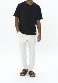 Svart bomullströja med korta ärmar, kombinerad med lätta vita byxor och bruna sandaler med spännen.