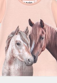 T-shirt rosa claro com uma estampa detalhada de duas cabeças de cavalos, uma cinza e outra castanha, com uma textura suave e um decote redondo.