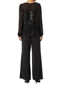 Schwarzes Oberteil mit besetztem Rücken, langen transparenten Ärmeln, kombiniert mit weiten schwarzen Hosen. Glatte Textur, elegantes Design.
